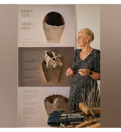 Maria van Kempen van Anno-Art op haar expositie, naast een poster met haar ringen